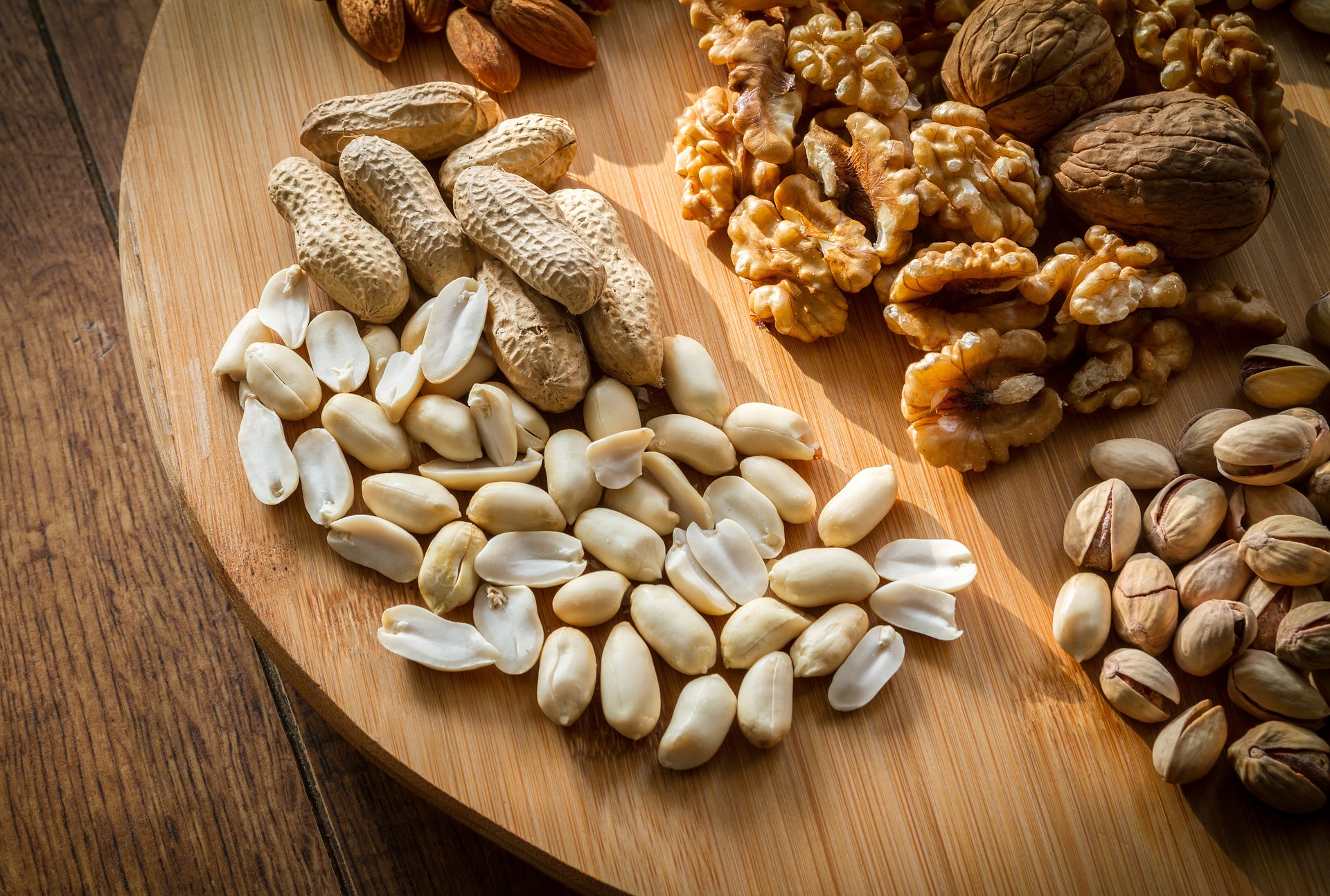 Assorted premium nuts including peanuts, walnuts, pistachios and almonds on a wooden board